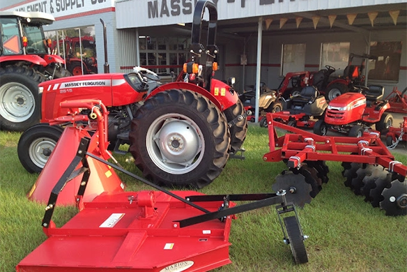Massey Ferguson tractor and multiple red farm implements displayed outside Watts Bros Implement and Supply showroom