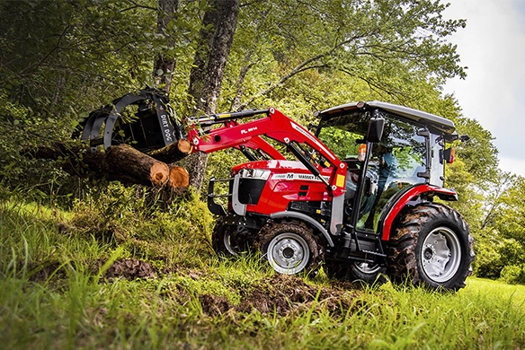 Massey Ferguson 2800M Series tractor using a front loader attachment to move logs in a wooded area.