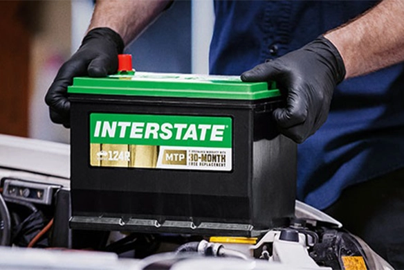 Service technician holding an Interstate battery, preparing for installation.